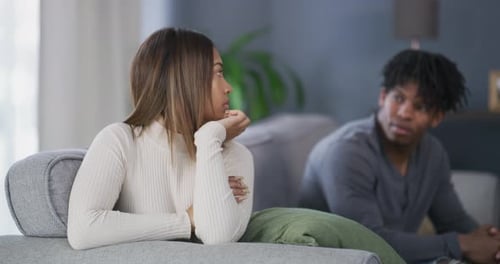 Pensive Woman on Sofa with Man in Background