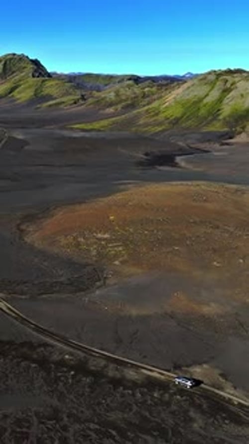 Vertical drone aerial of a lone SUV on a dirt track across black volcanic plains with a rusty