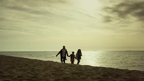 Family holding hands running on beach at sunrise