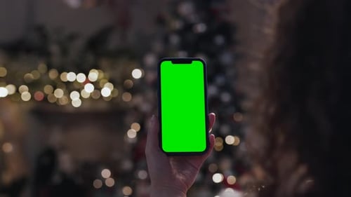 Woman holding green screen smartphone in christmas decorated home in Russia