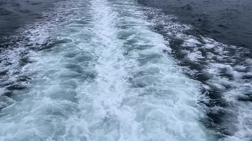 Boat wake trailing across deep blue ocean waters on a cloudy day, creating foamy white patterns
