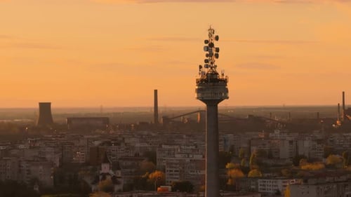 Aerial close up tracking shot ov a TV tower, sunset warm light, city and sky in the background, 4K50