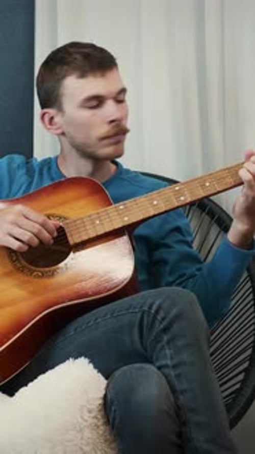 Young Adult Man Plays Acoustic Guitar at Home