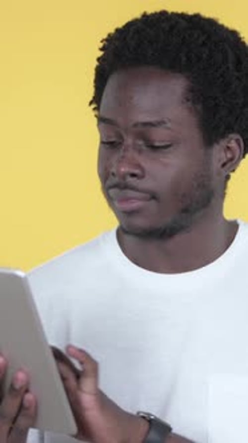 Young Man Using Tablet on Yellow Studio Backdrop