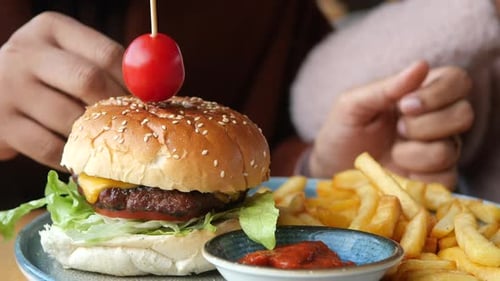 Hand Holding Beef Burger on Table Close Up