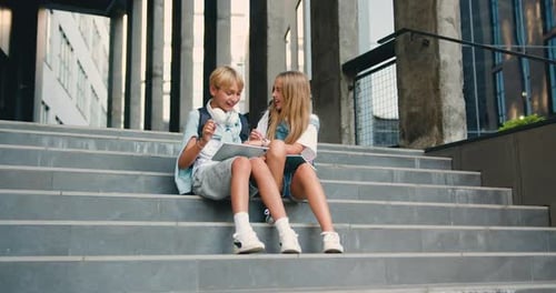 Happy schoolchildren sittingding near school building on the stairs, having fun, talking