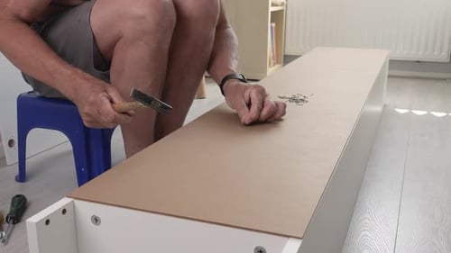 Ein erwachsener Handwerker hämmert die Nägel, während er zu Hause einen Schrank zusammenbaut.