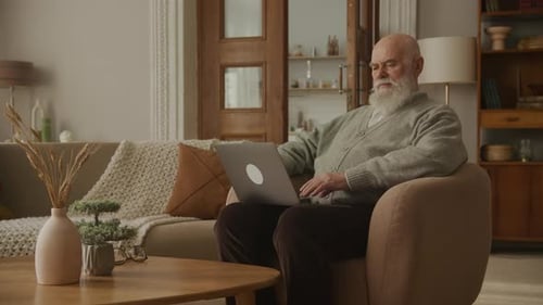 Senior Man Uses Laptop While Relaxing in Armchair