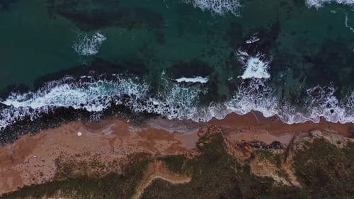 Waves crash on shore at sandy beach during sunny day near ocean