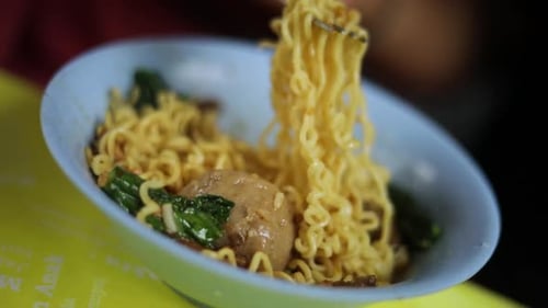 Shot of someone eating their indonesian food and playing with their noodles. The meal is fried noodl