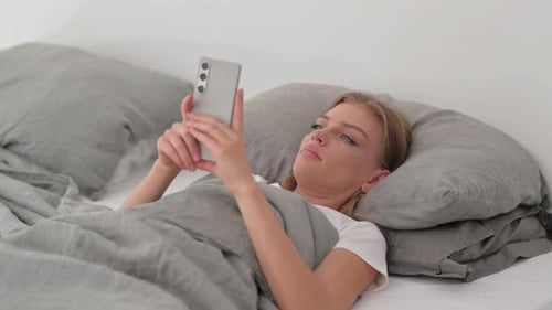 Woman Using Phone While Relaxing in Bed