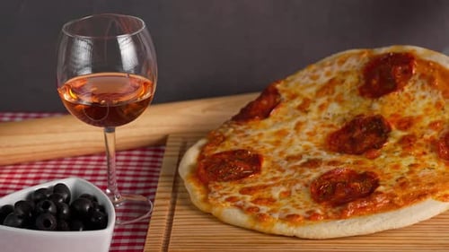 Freshly Baked Pepperoni Pizza On A Wooden Board With Rose Wine On The Side And Black Olives