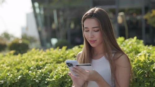 Portrait of Woman Buys Goods Online with Credit Card and Smartphone in City Park