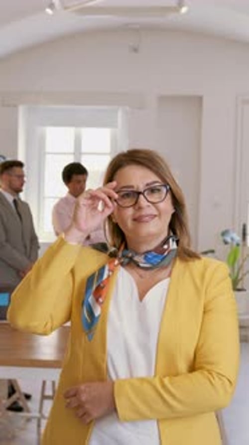Portrait of smiling businesswoman in office with her colleagues in background.