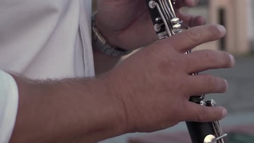 Musician in a white shirt plays the clarinet. Pan up. Close up. Truck in the background out of focus