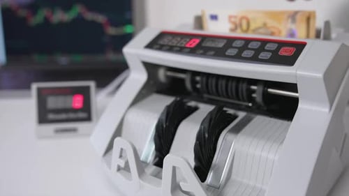 Die Hand legt ein Bündel mit fünfzig-Euro-Scheinen in einen Schlitz einer Geldzählmaschine.