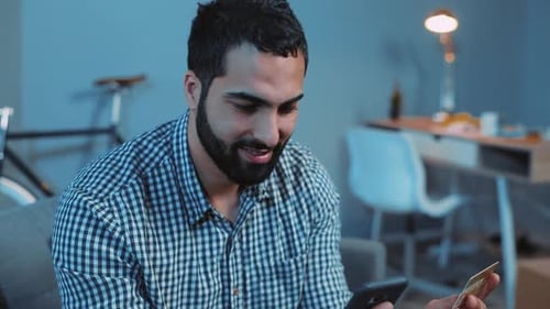Man Using Credit Card and Phone Indoors