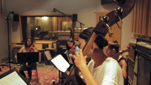 Woman Playing the Upright Base with Orchestra in Background at the Studio