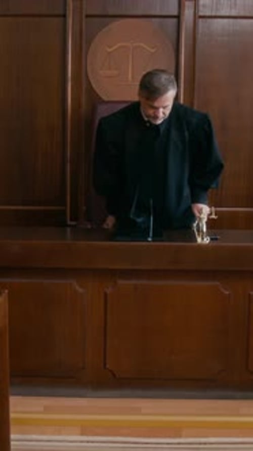 Middle-Aged Male Judge Entering Courtroom and Sitting Down at Bench