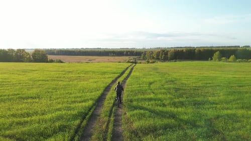 Aerial View of a Man Cycling Along a Country Road and Grassy Field The Man Rides a Bicycle in the