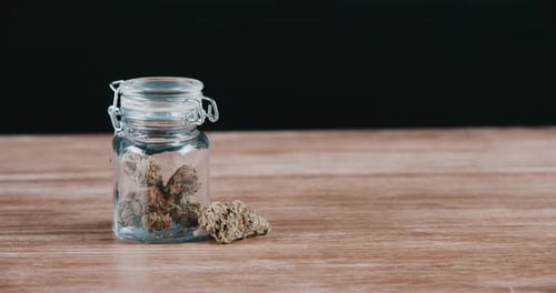 4k video footage of dried marijuana stored in a glass bottle against a black studio background