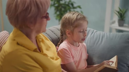 Girl Reads With Mature Woman on Sofa Indoors