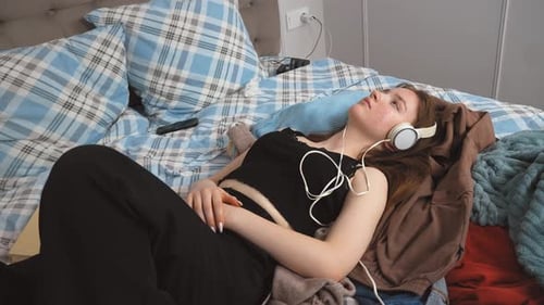 Young Woman Relaxing, Lying on Bed with Headphones