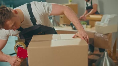 CloseUp of Employee Worker Sealing Cardboard Box Using Duct Tape Machine