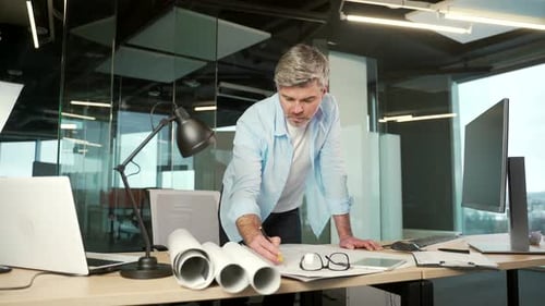 mature creative designer, architect working in the office at work a computer desk with drawings.