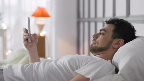 Man Using Smartphone While Lying in Bed
