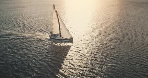 Magnifique voilier naviguant au coucher du soleil sur l'eau calme et dorée de l'océan