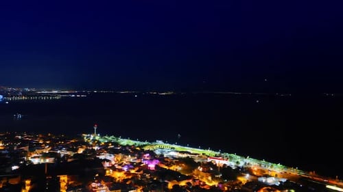 Illuminated scenery of the city divided by the dark waterscape. Boat moves by the sea