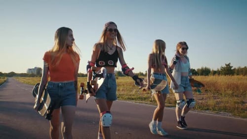 Women Friends Carry Skateboards and Stroll Along Paved Road
