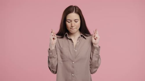 Hopeful Woman with Fingers Crossed on Pink Background
