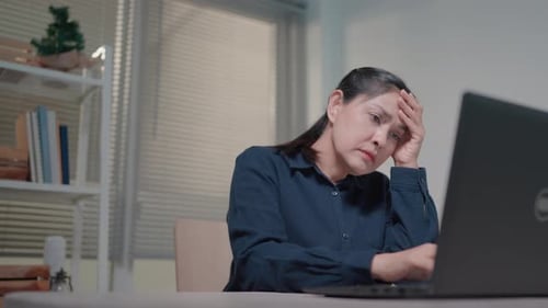 A woman is upset that the computer is broken or running slowly, sitting at the table looking at the