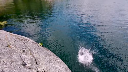 Junger weißer Mann springt in Zeitlupe von einer Felsklippe in den Blue Lake, eine breite Pfanne über ihm. Männlicher Schwimmer