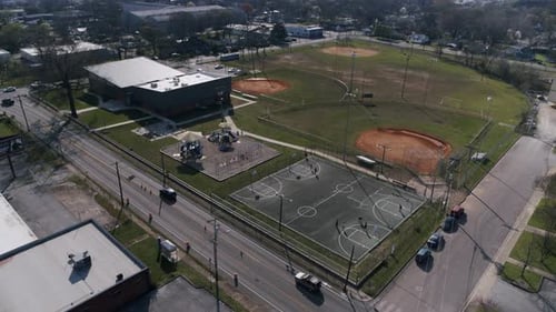Aerial pan across a recreation field with basketball courts and playground equipment being used by p