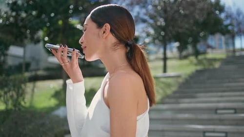 Smiling Girl Recording Audio Message on Modern Smartphone Standing Sunny Street