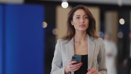 Woman with Smartphone Walks in Modern Office Lobby