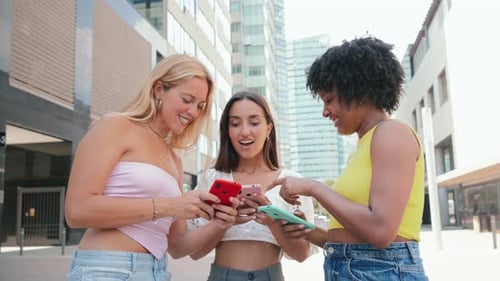 Three Young Women Use Smartphones Outdoors in City