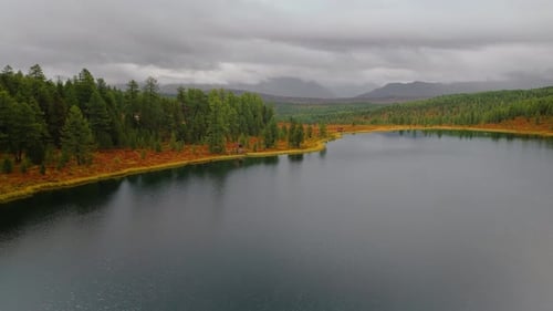 Beautiful aerial view of Altai lake with forested hills and autumn scenery. Roadside houses visible