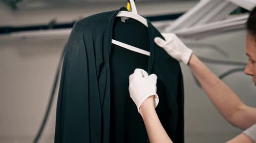 Close Up Professional Dry Cleaning Young Girl Irons a Black Sweater on Hanger with Steam