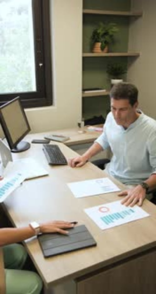 Vertical video: Diverse coworkers receiving charts and marking graphs analyzing data at office desk