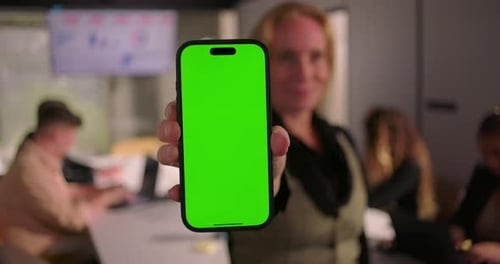 Vertical smartphone with green screen held by businesswoman in modern office,