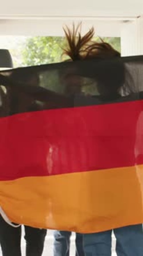 Vidéo verticale : Entrée d'un trio décontracté accueillant l'hôte à la porte, brandissant un drapeau avec un téléphone, des boissons