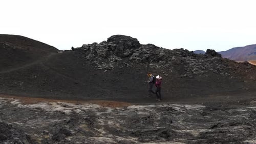 Aerial tracking shot of a couple hiking the black volcanic mountains in Iceland