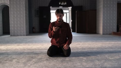 Front view of Muslim bearded man sitting in mosque reading Quran on phone, religious book with Arabi