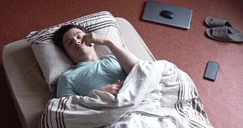 Un jeune homme adulte se réveille sur un matelas au sol, sommeil agité, vue d'en haut