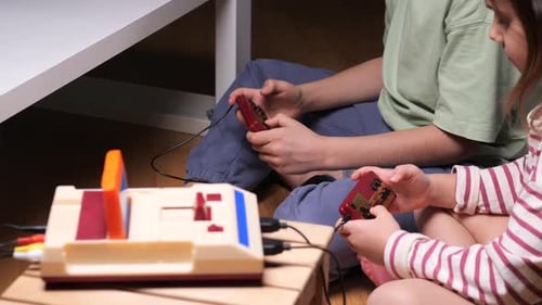 Duas crianças brincando com um console de jogos retrô em casa