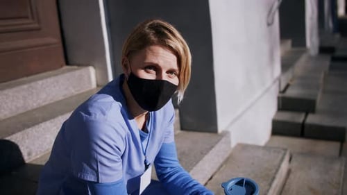 Female Medical Worker in Mask Sits Outside Building